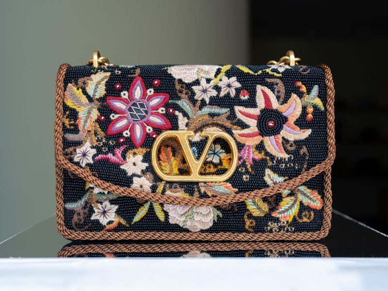 A designer handbag with floral embroidery and a prominent gold logo, showcasing classic luxury style.