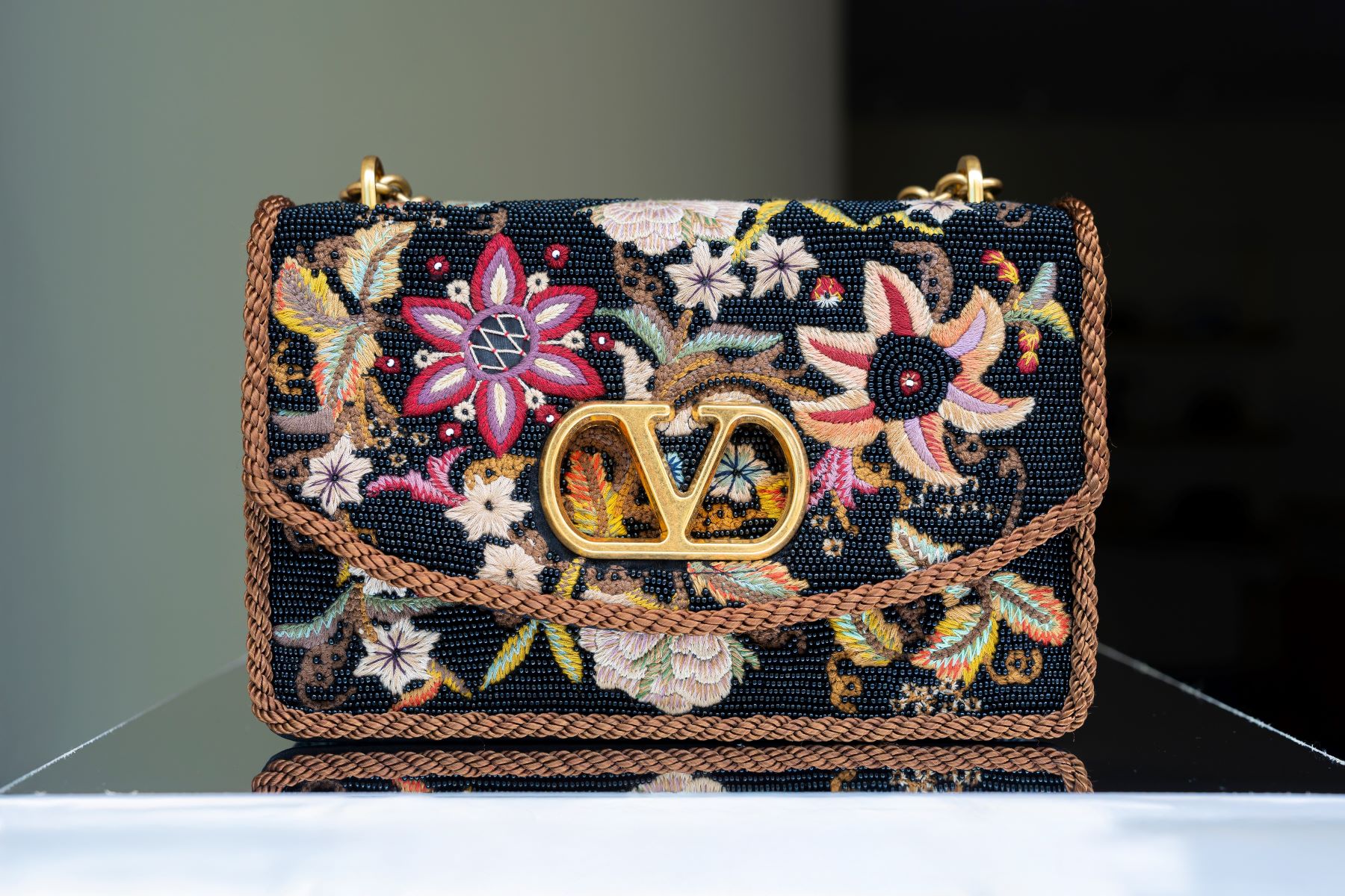 A designer handbag with floral embroidery and a prominent gold logo, showcasing classic luxury style.