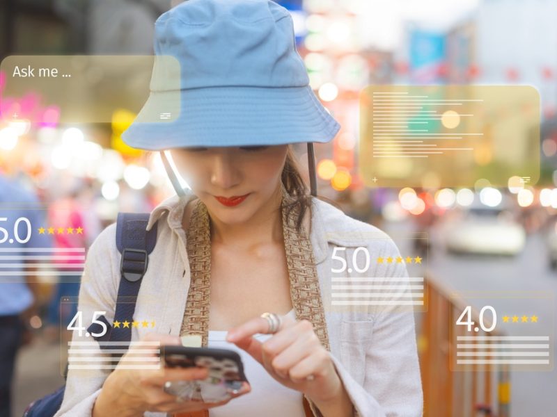 A woman with a blue hat checks her phone in a bustling street, with star ratings and prompts displayed around her.