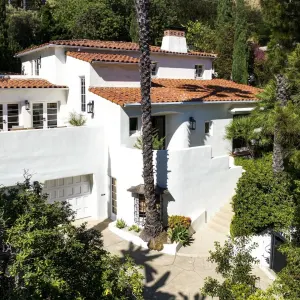 A stunning 1931 Spanish Revival home featuring white stucco walls, red tile roofing, and lush surrounding landscaping.