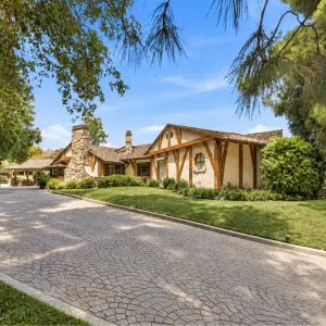 Charming Hollywood estate with stone accents and a winding driveway, set against a backdrop of lush greenery.