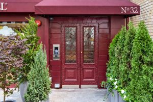 Elegant red double doors with detailed designs, framed by lush greenery and a maroon awning, showcasing the townhouse's charm.